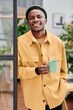© pressmaster - Young successful African American businessman with cup of coffee standing in front of camera against openspace office