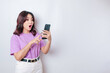 Surprised Asian woman wearing lilac purple t-shirt pointing at her smartphone, isolated by white background
