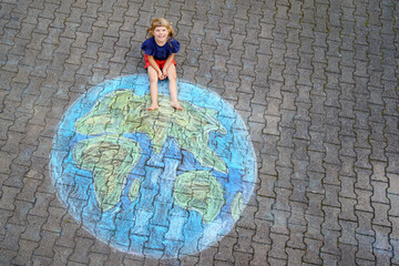 Little preschool girl with earth globe painting with colorful chalks on ground. Positive toddler child. Happy earth day concept. Creation of children for saving world, environment and ecology.