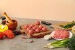 © Pixel-Shot - Cutting board with raw meat balls, plate of mince, spices and vegetables on table near beige wall