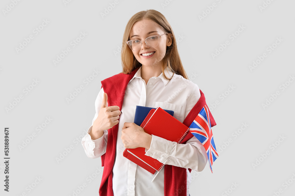 Young woman with UK flag and books on light background