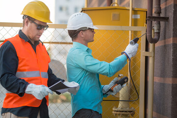 young men are standing near a gas pipe with an analyzer, wearing helmets, glasses, gloves. checking for gas leaks.