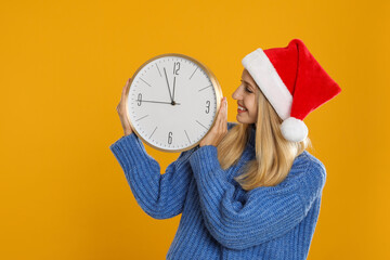 Wall Mural - Woman in Santa hat with clock on yellow background. New Year countdown