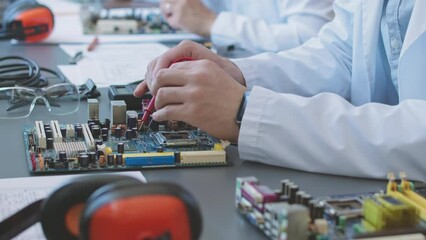 Unrecognizable electronics engineer soldering motherboard parts at desk in laboratory