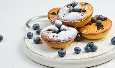 Canvas Print - Round mini cottage cheese pies with blueberries on a white wooden board, delicious sweet dessert