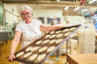 © Robert Kneschke - Older woman as a baker carries baking sheet with butter plaits