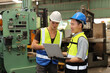 © feeling lucky - Technician engineer in protective uniform with hardhat standing and teaching apprentices or colleague worker to use computerized machine control at heavy industry manufacturing factory