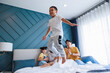 Boy jump on bed show his family parent, sister and grandmom cheerful him together at bedroom.