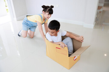 Wall Mural - Cute asian sister play with brother, boy having fun riding in box in new house. Moving day.