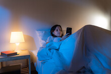 Girl Looking Her Smart Phone Doom Scrolling On Bed In The Middle Of The Night. Technology At Bed Concept.