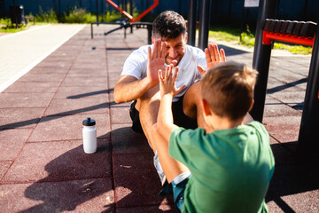 Wall Mural - Father and son after training, resting on the open gym floor, throwing 5 to each other