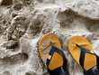 Yellow slipper put on sand ground at the beach. Rough surface texture in nature. Human relaxation on vacation.