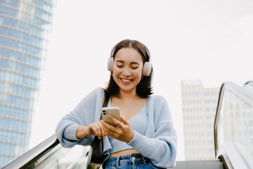 Wall Mural - Young beautiful asian smiling happy girl in headphones with phone