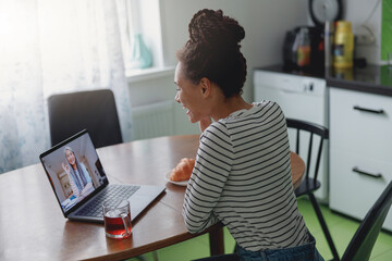 Wall Mural - rear of joyful smiling woman speaking on video call with senior woman sitting in kitchen