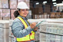 African Female Manager With Checklist Document Checking Stock Smiling To Camera In The Warehouse Distribution. Woman Worker In Safety Uniform Working For Logistic Business.