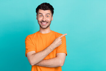 Poster - Photo of young handsome bearded bristle positive man wear orange t-shirt finger pointing empty space offer toothy beaming isolated on cyan color background