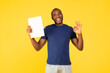 © Prostock-studio - Cheerful Black Guy Holding Paper Gesturing Okay Over Yellow Background