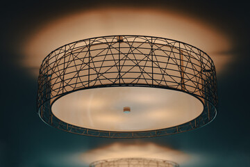 A glowing and lit drum light with black metal accents on a warm ceiling