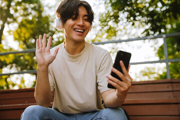 Wall Mural - Young handsome smiling asian boy in headphones holding video conference