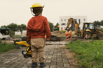 Child with excavator near construction site, dreams to be an engineer. Little builder. Education, and imagination, purposefulness concept