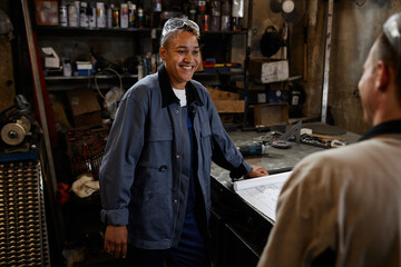 Portrait of smiling female worker talking to coworker in industrial workshop while discussing project