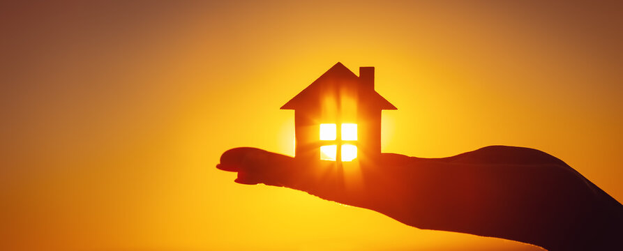 Fototapete - Woman's hand holding a model of a house on sunset evening