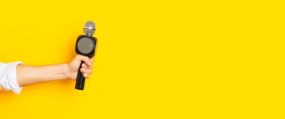 Man's hand holds a microphone in a hole in a torn bright yellow cardboard background. Banner