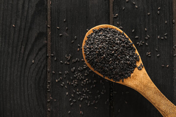 Spoon with black sesame seeds on dark wooden background, closeup