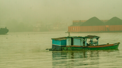 Sand miner activity at Mahakam River, Samarinda in the morning. Wooden boat take up the sand from the bottom of Mahakam River in the morning with barge of coal in the background.