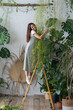 © DimaBerlin - Young happy joyful German female plant lover standing on stepladder and embracing asparagus fern houseplant, enjoying plant care and home gardening, spending time in nature and growing tropical plants