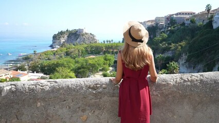 Wall Mural - Smiling traveler woman turns around enjoying panoramic view of Tropea village on the Coast of the Gods, Calabria, Italy