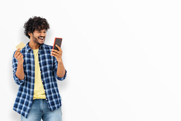 Smiling happy Asian man with curly hair holding mobile phone and credit card standing on white background, online shopping concept, copy space