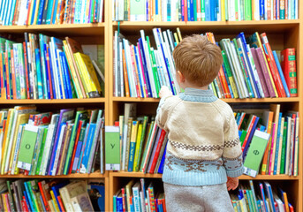 a small child is drawn to knowledge. a boy in a public library chooses a book for himself.