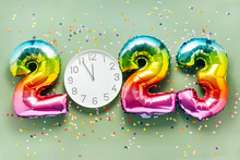 Colorful Bright Air Balloon Numbers And White Watch At 12 O'clock On Light Green Background With Confetti. 2023 New Year Concept Celebration