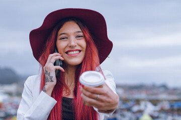 Wall Mural - smiling young woman talking on the phone and having a coffee to go