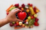 Fototapeta  - Serce trzymane w dłoniach na tle różnokolorowych owoców, dbanie o zdrowie, dieta złożona ze świeżych ooców