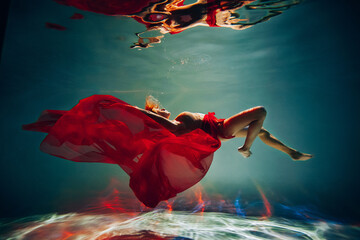 Art work. A slender, tanned girl with an athletic figure and blond hair, with red material and light underwear, dives and spins underwater in the pool. Aesthetic image for your design or decoration.