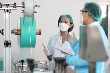 Canvas Print - Inspector man and colleague woman working on quality of mask and medical face mask production line, Industry and factory concept.