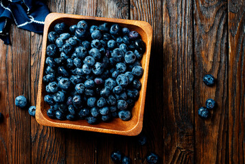 Poster - Freshly picked blueberries in wooden bowl. Juicy and fresh blueberries with green leaves on rustic table. Bilberry on wooden Background. Blueberry antioxidant. Concept for healthy eating and nutrition