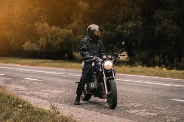 Wall Mural - male motorcyclist in a warm jacket and helmet in cold autumn weather on the road with a motorcycle cafe racer