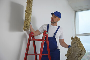 Wall Mural - Construction worker with used glass wool on stepladder in room prepared for renovation