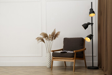 Wall Mural - Stylish armchair with book, floor lamp and spikes near white wall indoors, space for text. Interior design