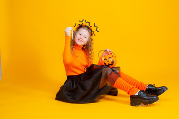 a teenage girl in a witch costume on a yellow background, holding a confent pumpkin eating marmalade worms halloween party