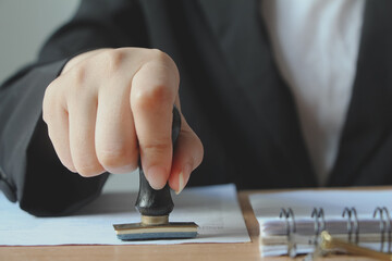 Business woman stamping with approved stamp on document paper at desk in office