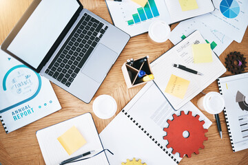 Documents, finance and report with a laptop, gear and paperwork on a table or desk in a corporate office from above. Notepad, stationery and graphs on a wooden surface in a workplace for planning