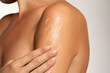 Close up young woman smearing shoulder with cream