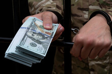 A Handcuffed Soldier Holds Out A Wad Of $100 Paper Bills From Behind Bars, Close-up, Selective Focus. Concept: Bribery, Bail.