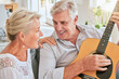 © Jade Maas/peopleimages.com - Senior couple with guitar for music and singing together on sofa for retirement lifestyle and summer lens flare. Happy elderly woman or creative musician people in living room home playing love song