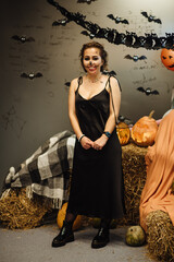 Young sexy fun gothic girl celebrating Halloween. Portrait of a dead girl among pumpkins with candles. Makeup for Halloween. Halloween season mood.