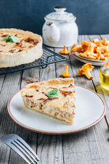 Homemade quiche or tart with chanterelles on rustic wooden background.